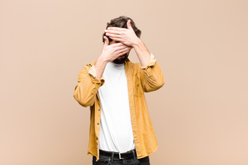 young crazy cool man covering face with both hands saying no to the camera! refusing pictures or...