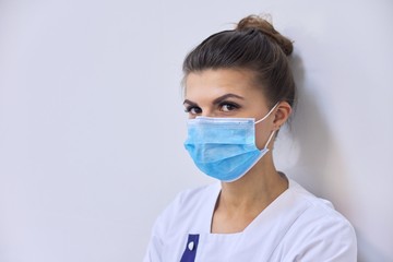 Young serious woman doctor in medical mask looking at camera