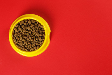 Yellow bowl with cat food on a red background. The concept of healthy eating for a pet. Copy space.