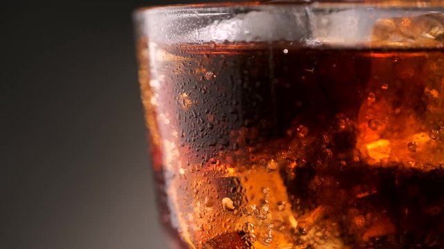Cold cola in a glass with ice rotates around its axis, macro. Bar background.
