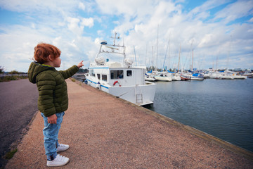 cute child on the pier looks at the moored yachts in yacht club