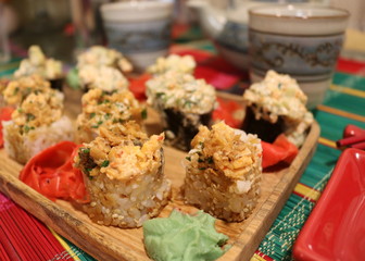 Two rice rolls with sesame seeds and delicious filling on top of the Board on the background of other rolls and Oriental cups.