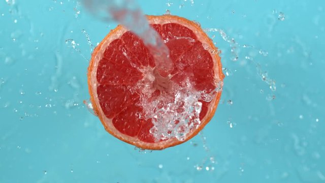 Water spinning off grapefruit on blue background.  Shot in slow motion with Phantom Flex 4K camera.