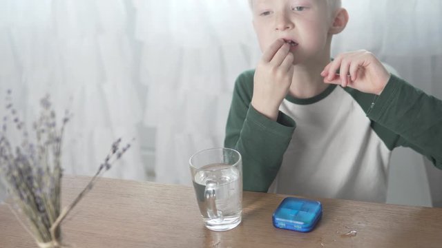 Blonde boy eats vitamin at home in the kitchen