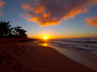 Beautiful Sunset over the ocean and beach with waves moving to shore and foot prints in the sand