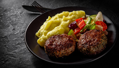 burger with mashed potatoes and vegetables salad on a black plate on Dark grey black slate background