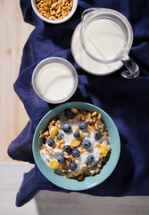 Bowl with oatmeal, corn flakes, blueberries and a glass of milk on a white wooden background