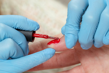 Manicurist covering nail with red gel polish. Manicure process in a beauty salon.