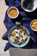Bowl with oatmeal, corn flakes, blueberries on a white wooden background