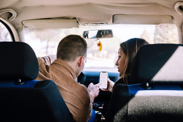 Stock photography of young couple inside the car consulting the smartphone. Scene from the back of the car.