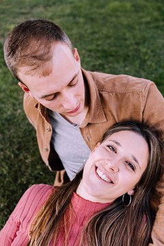Stock photography of young couple in affectionate attitude kissing and showing love sitting on the grass.