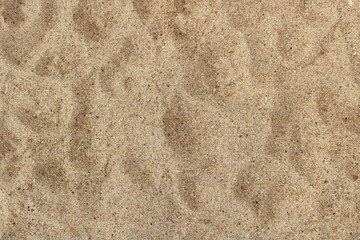 irregular surface of thin beach sand with pebbles, and shoe footprints - texture background view from above