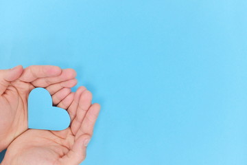 Blue heart shape cutout on hands in blue background. Top view, kindness and charity concept.