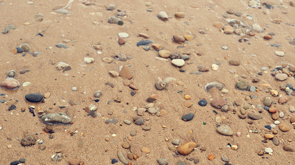 texture of wet sand of a beach with round colorful stones next to the sea