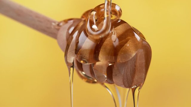 Honey dripping off honey dripper on yellow background