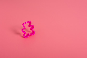 Pink plastic cookie cutter for making cookies in the shape of a teddy bear on a pink background. Culinary concept. Flat lay with copyspace.