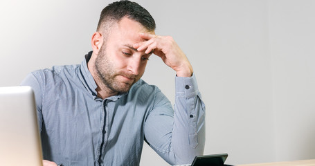 Frustrated businessman under stress nervously filling 1040 tax form with calculator at office desk.