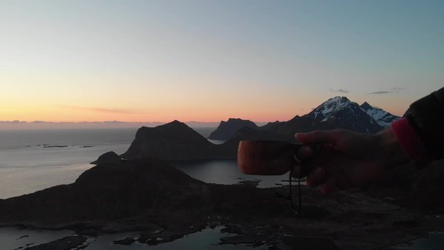 Holding a Kuksa in front of Lofoten Mountains at the summit in offersoykammen with a pan to the left