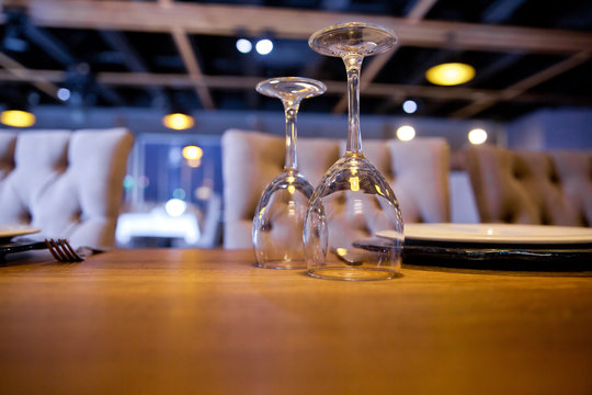 Empty outdoor restaurant table, Inverted empty glasses on the table. Tableware on table in cafe, focus on bakal stem . empty inverted glass on the wooden table .