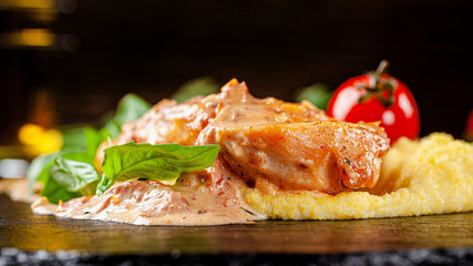 European, Italian cuisine. Roasted chicken fillet with corn porridge, with cherry tomatoes and basel. Serving dishes in a restaurant on black slate. background image, copy space