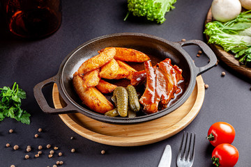 Pork ribs in a marinade, with rustic fried potatoes, and pickled pickles. Serving dishes in a restaurant in a cast-iron pan. background image, copy space text
