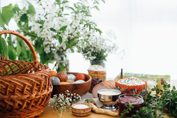 Easter eggs natural dyed, easter bread, ham, beets, butter, green branches and flowers on rustic wooden table with wicker basket and candle. Traditional Easter Food for blessing in church