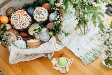 Traditional Easter basket for blessings in church. Easter modern eggs, cake, ham, beets, butter in rustic basket decorated with green buxus branches and flowers on wooden table with candle