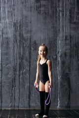Smiling girl gymnast posing near a black textured wall.