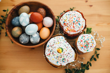 Homemade easter cake and stylish easter eggs natural dyed in wooden bowl on rustic table with flowers. Happy Easter. Traditional Easter bread. Flat lay