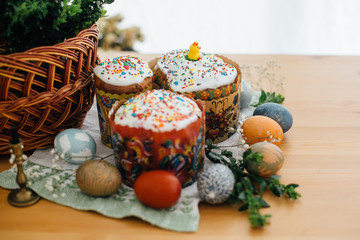 Traditional Easter food on rustic table. Homemade easter cake, easter eggs natural dyed, candle, green branches and flowers with wicker basket on wooden background. Easter Food for sanctify
