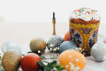 Homemade easter cake and stylish easter eggs natural dyed on rustic cloth with flowers and green brunches on table in light. Happy Easter. Traditional Easter bread. Copy space