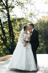 Loving wedding couple outdoor. Bride and groom. Wedding couple. Close up of a newlywed couple, a bride with a beautiful hair style and make up. Happy newlywed couple walking in the park.