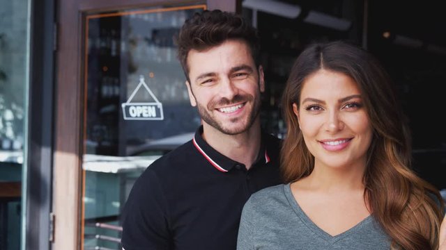 Portrait of hispanic couple owning start up coffee shop or restaurant standing in doorway - shot in slow motion