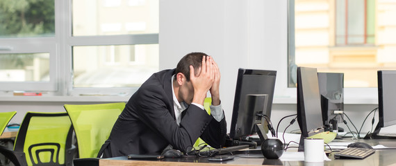 Portrait of sad and tired businessman in suit sitting with monitor computer in office room....