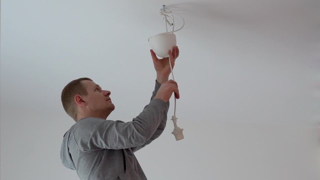 repair and home decoration. a man hangs a lamp in the room from the ceiling.