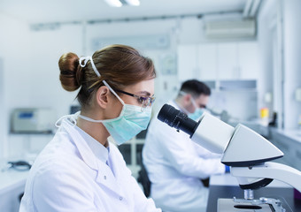 Biologists looking through microscope in laboratory