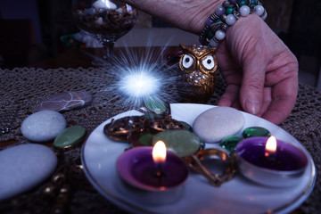 A woman's hand in bracelets lays out stones and amulets against the background of burning candles
