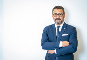A bearded businessman posing with his arms tied in his suit in front of the background