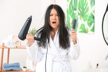 Stressed Asian woman with hair dryer at home