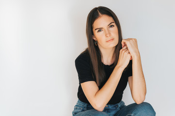 Indoor portrait of beautiful young woman, wearing black t-shirt and high waist jeans, posing on white background