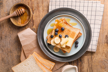 Tasty toasted bread with honey, butter and fruits on plate