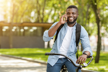 Smiling Black Guy Talking On Cellphone While Riding Bicycle Outdoors