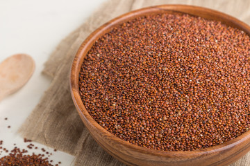 Wooden bowl with raw red quinoa seeds on a white wooden background. Side view, close up, selective focus.