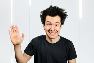 shaggy mad young guy freak with long hair, smile and welcome with a raised hand on white background.