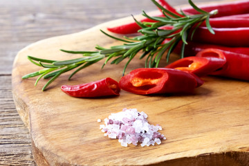 Red organic chili peppers on a wooden board. Nearby lies sea salt and a sprig of rosemary. Hot seasoning. Place for text