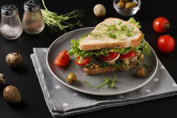 Sandwich with chicken, cherry tomatoes, quail eggs and microgreens against a dark background