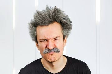 Portrait of jocular aging man wrinkles his nose from sour on his face in Einstein manner.