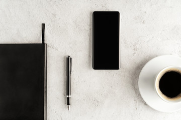 Up-to-date smartphone with notebook, fountain pen and cup of coffee on concrete background. Workstation concept flat lay. Coffee break top view. Mockup for your design.