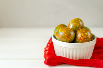 trendy modern easter multi-colored, originally painted, marble eggs in a white plate on a red silk towel on a light background with place for text