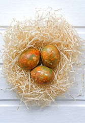 fashionable modern Easter multi-colored, originally painted, marble eggs in a nest on a white wooden background with place for text shot from above